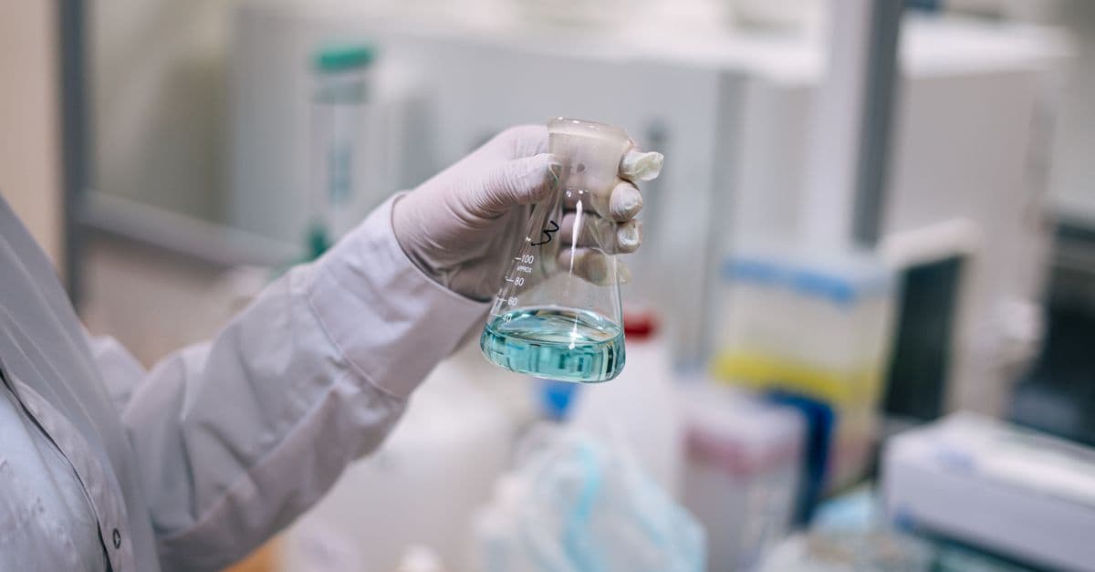 A scientist in a laboratory analyzing a fluid in an Erlenmeyer flask.