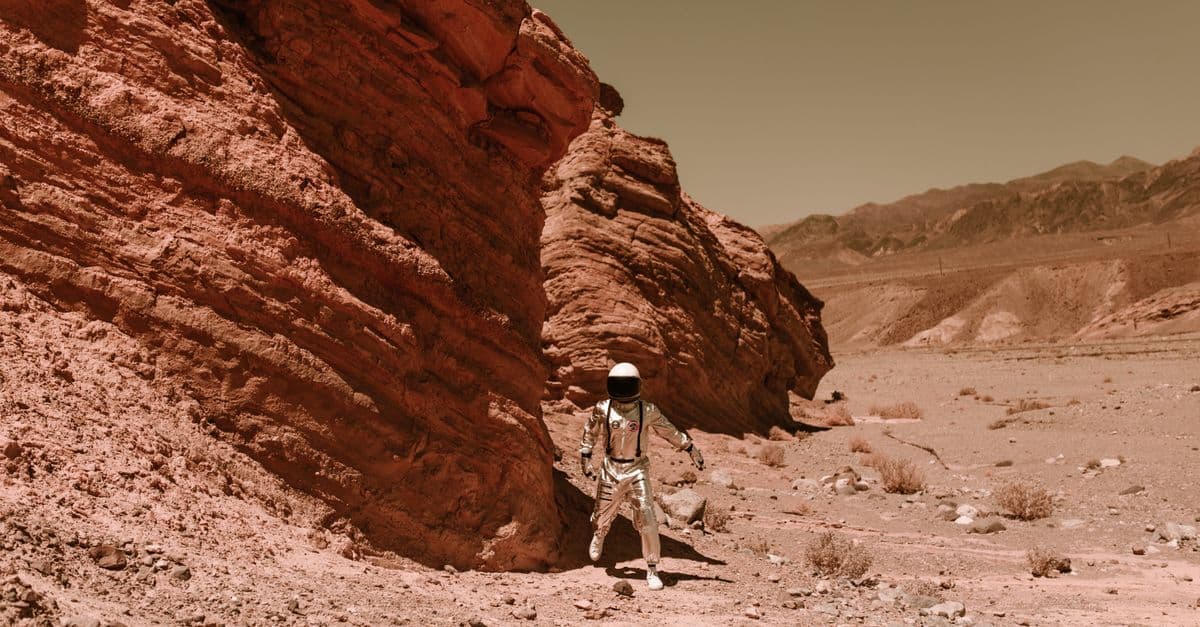 An astronaut in a spacesuit explores a barren, eroded desert, resembling Martian terrain.