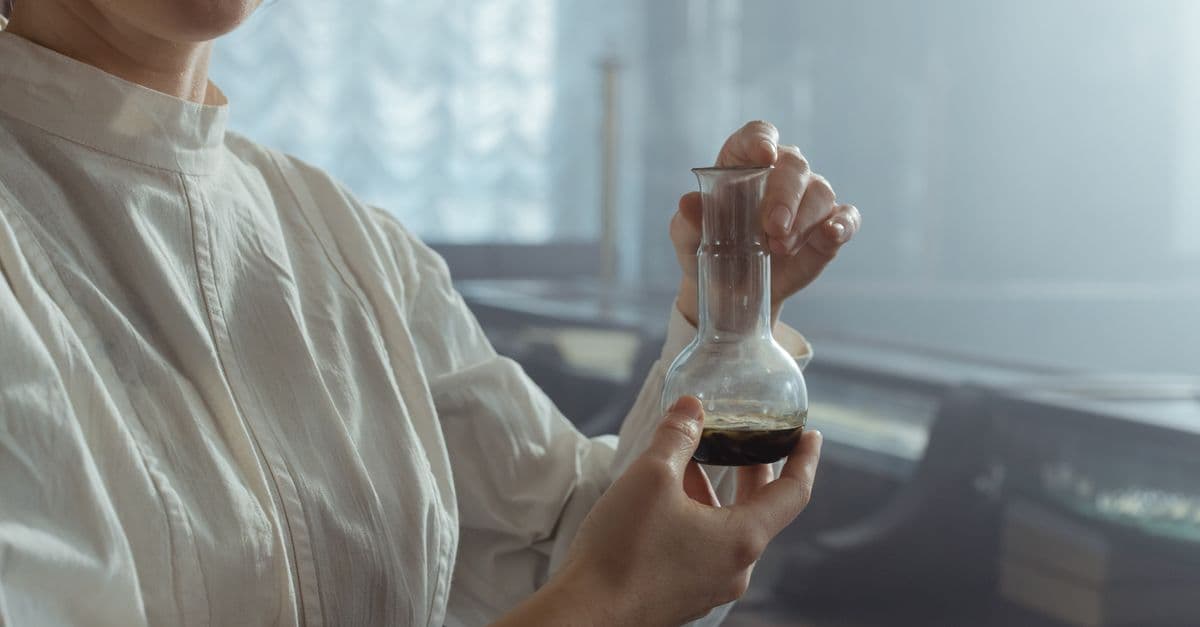 A woman in a white shirt delicately holds a glass flask in a softly lit laboratory.