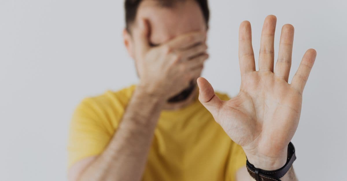 Close-up of a man covering his face and showing a stop gesture with his hand.