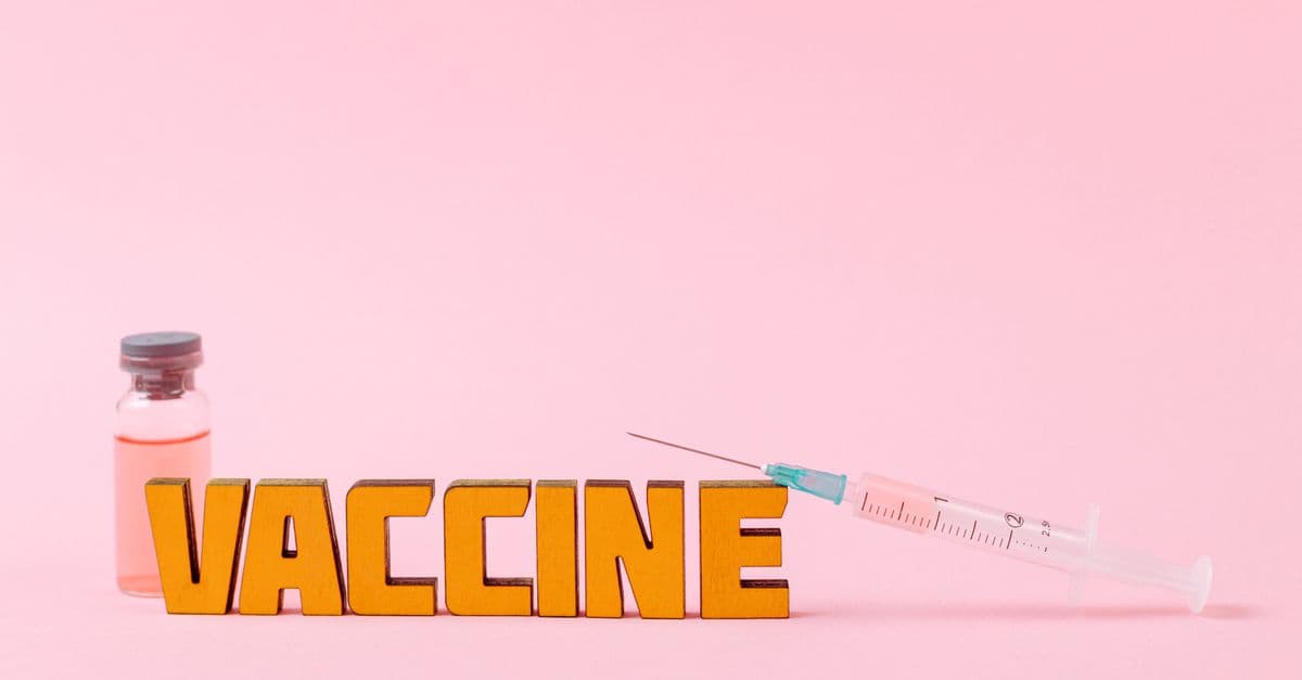 Close-up of a syringe and vaccine vial on a pink backdrop for health concepts.