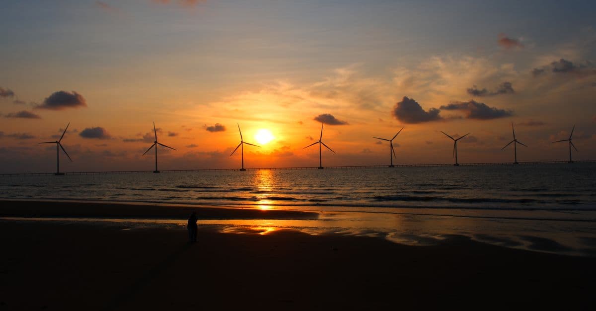 Silhouetted wind turbines against a vibrant ocean sunset create a serene coastal scene.