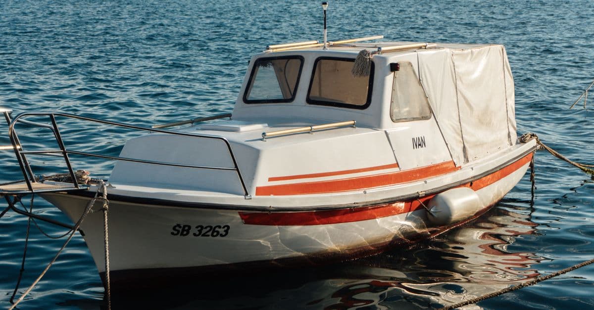 A white boat named Ivan moored on a tranquil water body, capturing a serene sunny day.