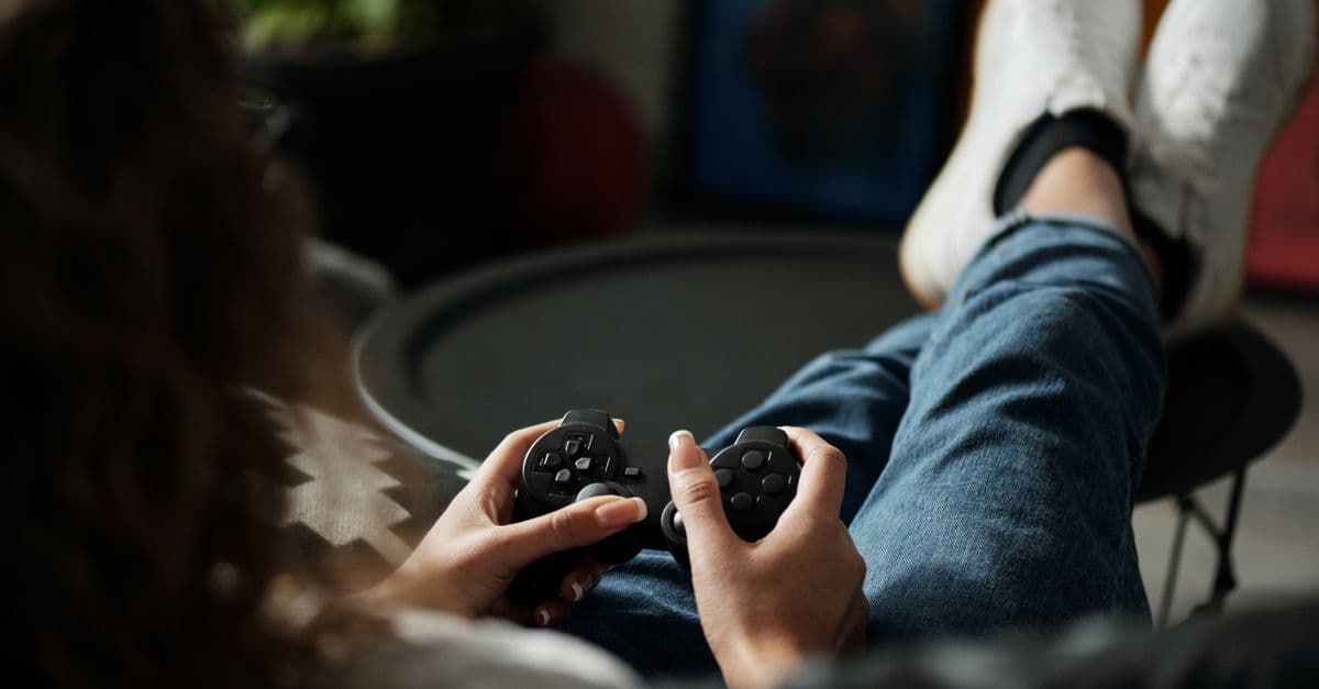 Close-up of woman gaming with a controller, feet propped up, enjoying leisure time indoors.