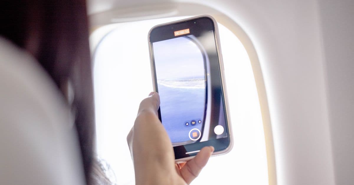 Woman filming out an airplane window using a smartphone, capturing a beautiful aerial view.