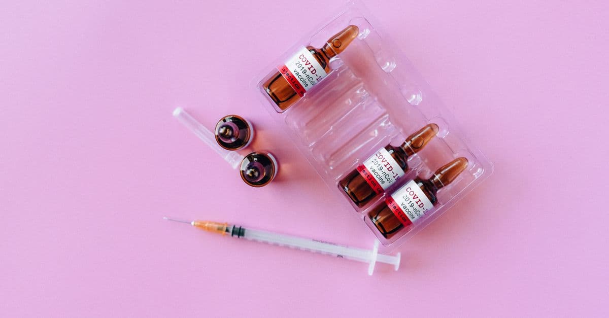 Top view of COVID-19 vaccine vials with syringe on a pink background, symbolizing vaccination and health.