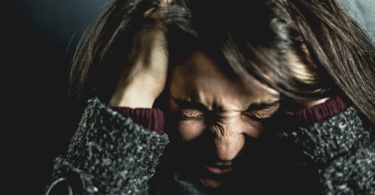 Close-up of a woman in distress with eyes closed and hands in hair, expressing anxiety.