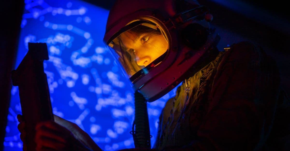 A woman astronaut examines a control panel with a star map background in futuristic blue lighting.