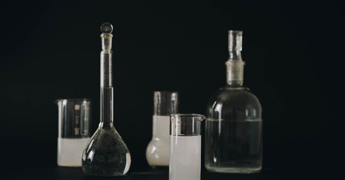 Close-up of various laboratory glassware filled with liquids on a dark background.