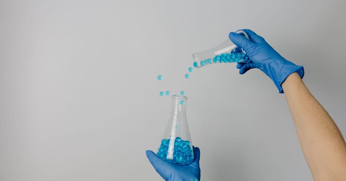 Hands in blue gloves transferring blue beads between beakers in a lab setting.