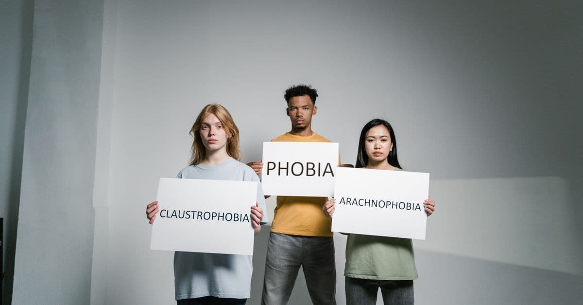 Three individuals holding signs representing various phobias, raising awareness.