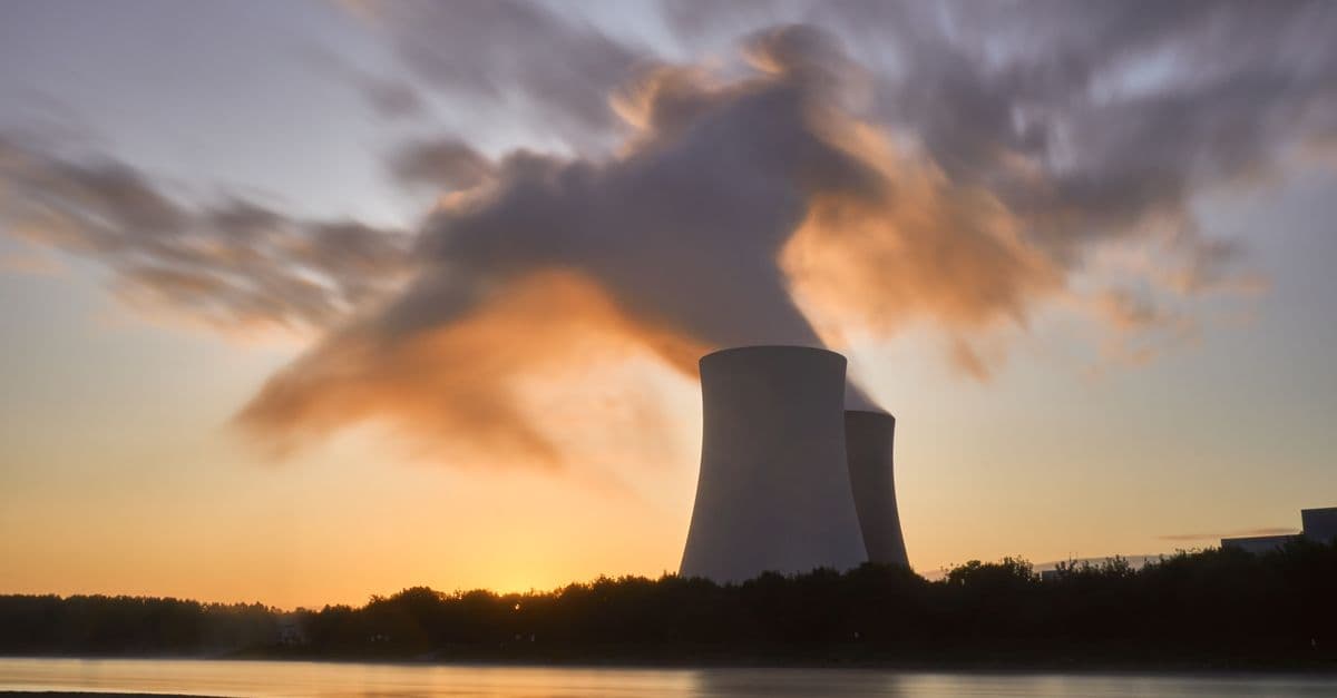 Dramatic image of a nuclear power plant at sunrise with steam rising into a colorful sky.