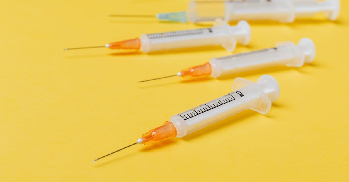 Medical plastic disposable syringes of different sizes with orange and green needle hubs placed on yellow background without protective cover