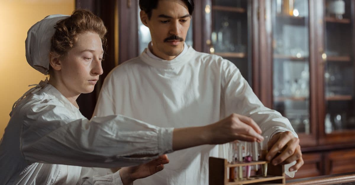 Pharmacists in historic attire work with test tubes in an antique laboratory setting.