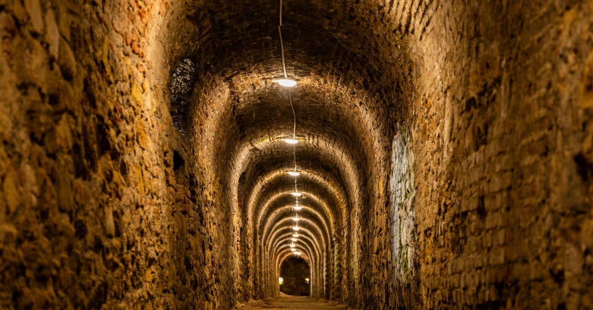 A dimly lit historic underground tunnel featuring brick archways, creating a mysterious ambiance.
