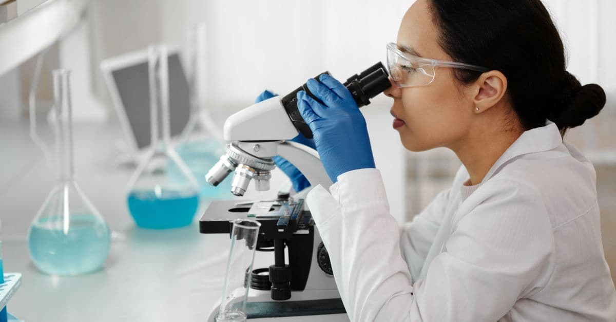 Female scientist in a laboratory examining samples through a microscope for research.