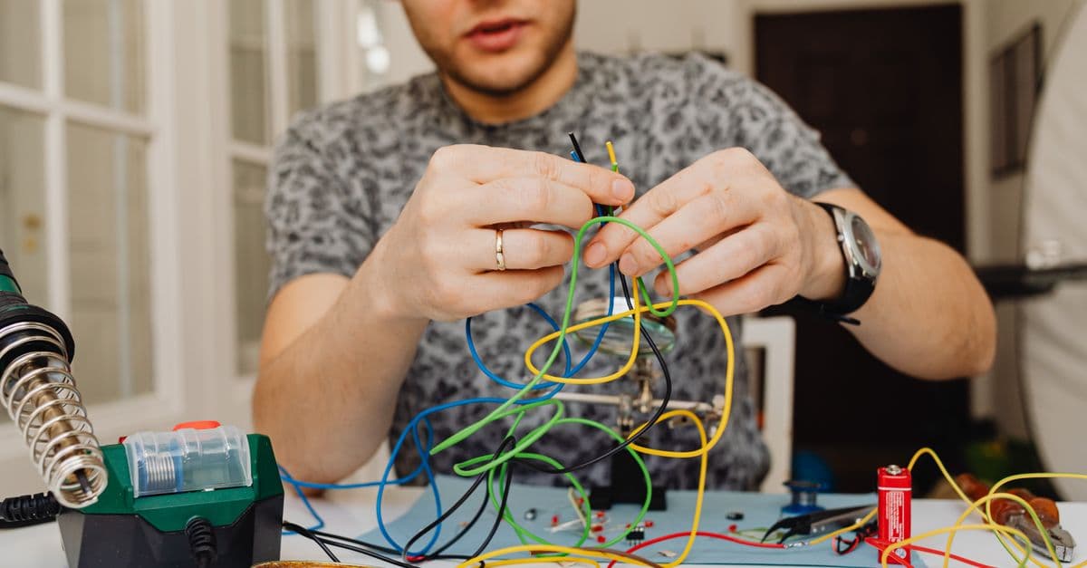 Caucasian man organizing colorful wires indoors with focus on electronics.