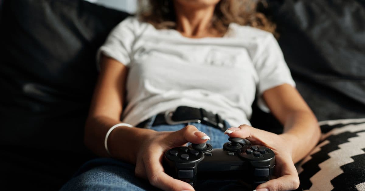 A woman relaxing on a sofa playing video games at home, focusing on a controller.