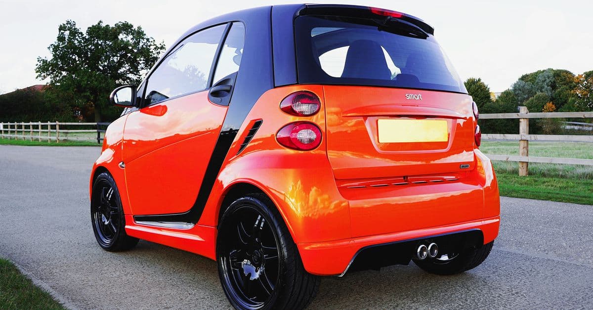 A vibrant orange Smart car is parked on a road in Knebworth, showcasing its sleek design.