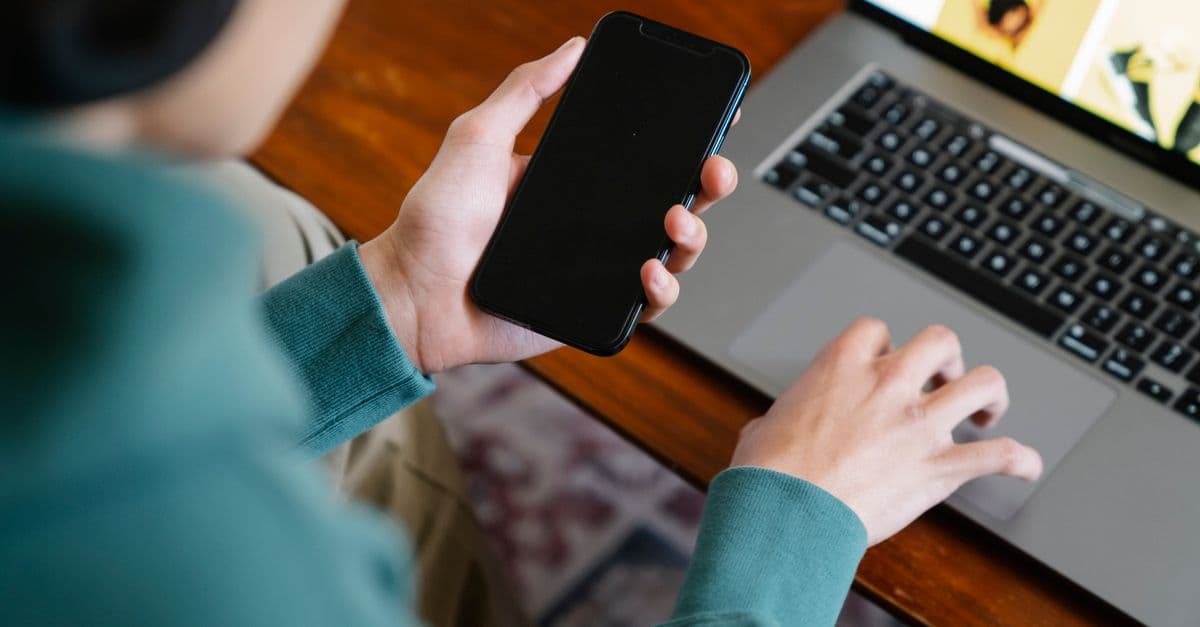 Close-up of a person multitasking using a smartphone and laptop, symbolizing modern remote work.