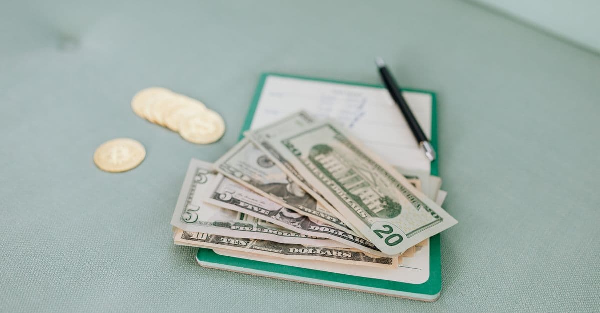 Close-up of American dollar bills and coins on a journal with a pen, representing budget planning.