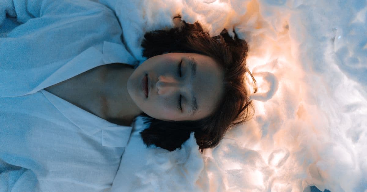 Tranquil portrait of a woman lying peacefully on cloud-like surroundings, evoking calmness.