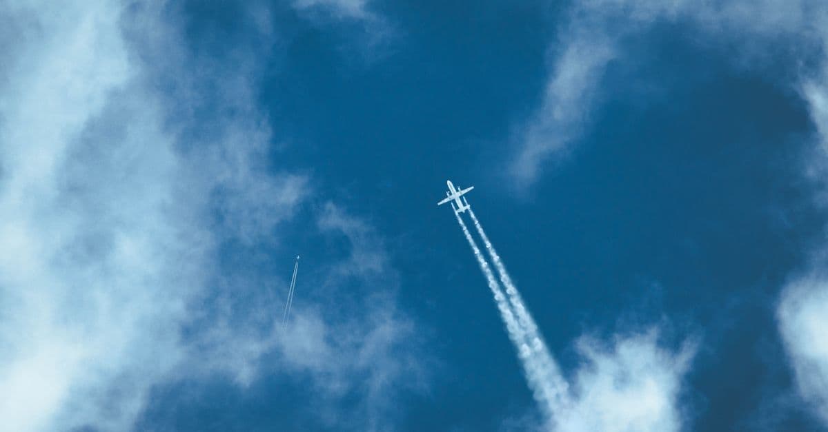 Airplane flying through a clear blue sky leaving a long contrail behind.