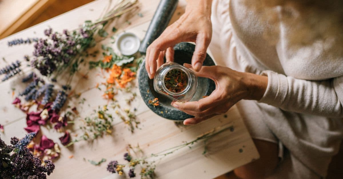 Hands preparing dried flowers and herbs in a mortar. Ideal for holistic and wellness themes.
