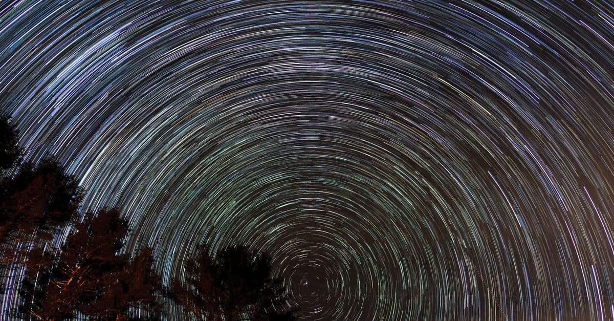 Mesmerizing long exposure shot capturing star trails over silhouetted trees, showcasing the beauty of the night sky.