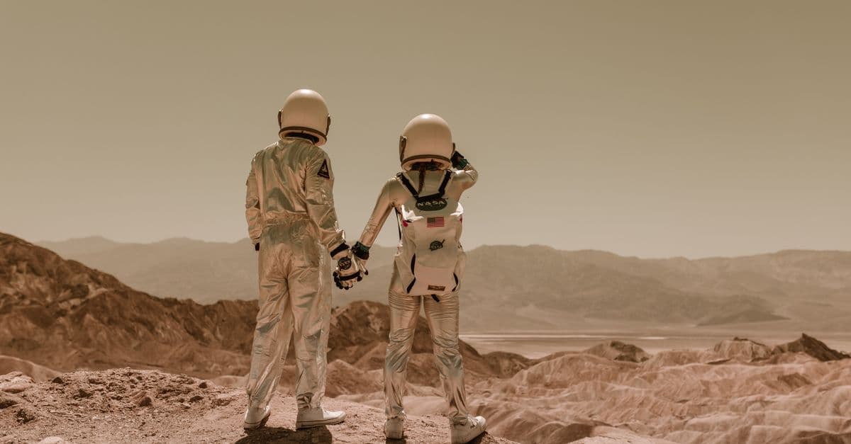 Two astronauts in space suits holding hands in a desert, Mars-like terrain.