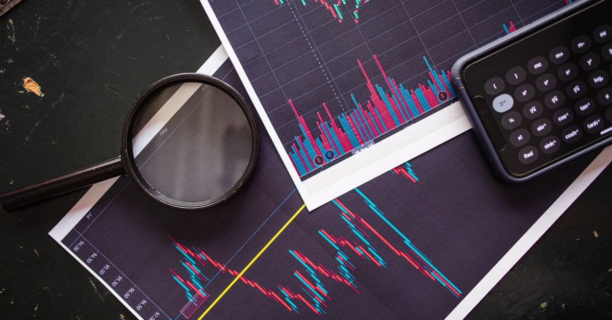 Stock market charts analyzed with a magnifying glass and calculator for financial research.