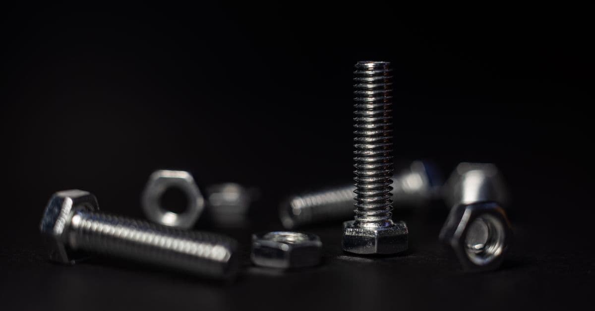 Detailed close-up of metal screws and nuts with a dark background highlighting textures and shapes.