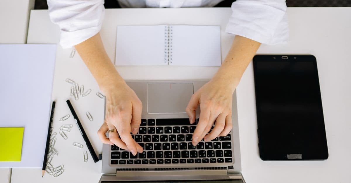 A workspace with a laptop, digital tablet, and hands typing, viewed from above.