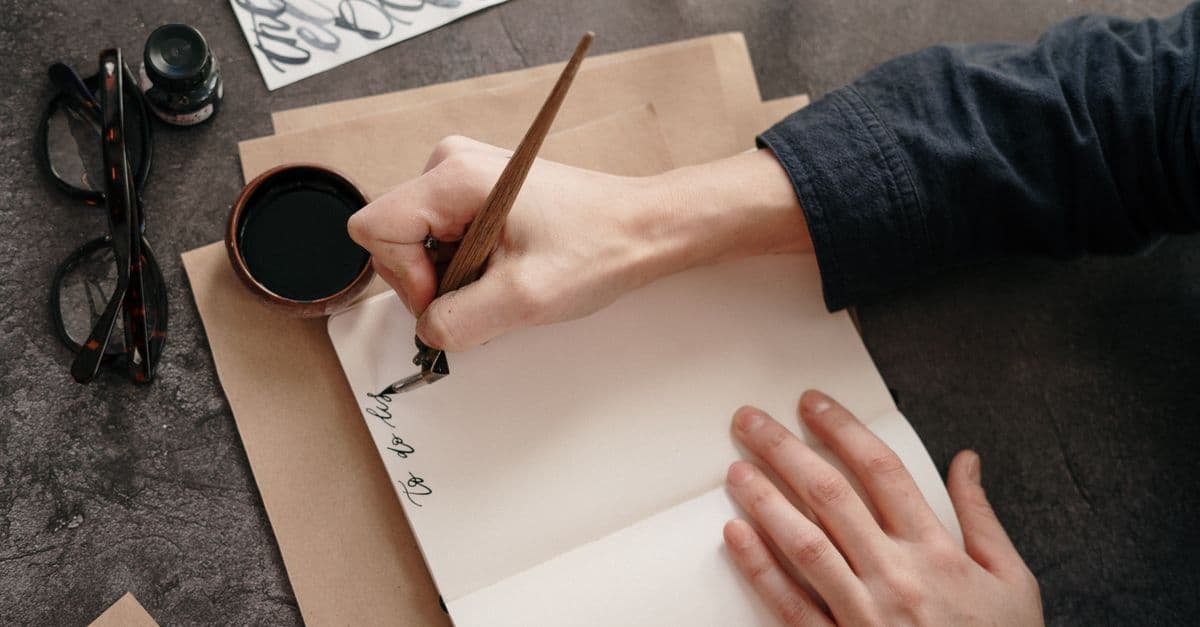A person's hand writing calligraphy in a notebook with ink and pen, showcasing artistic skill.
