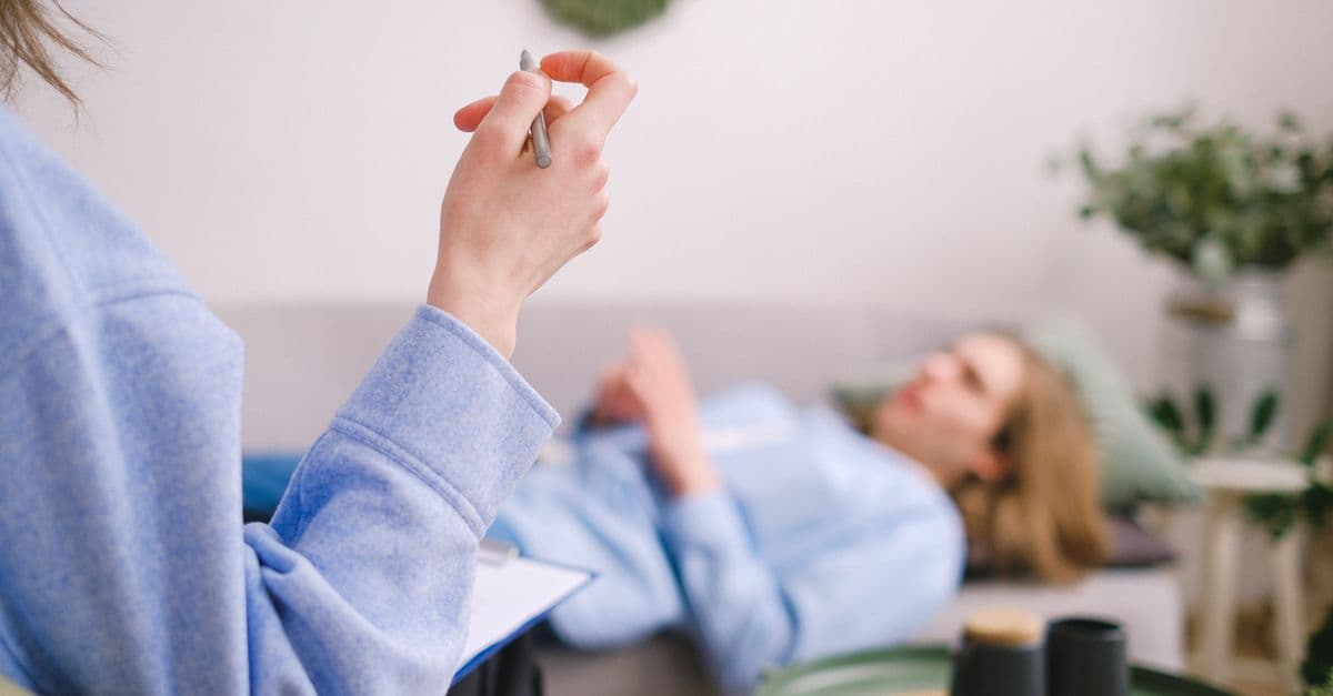 Therapist taking notes during a therapy session with a relaxed client lying on a couch.
