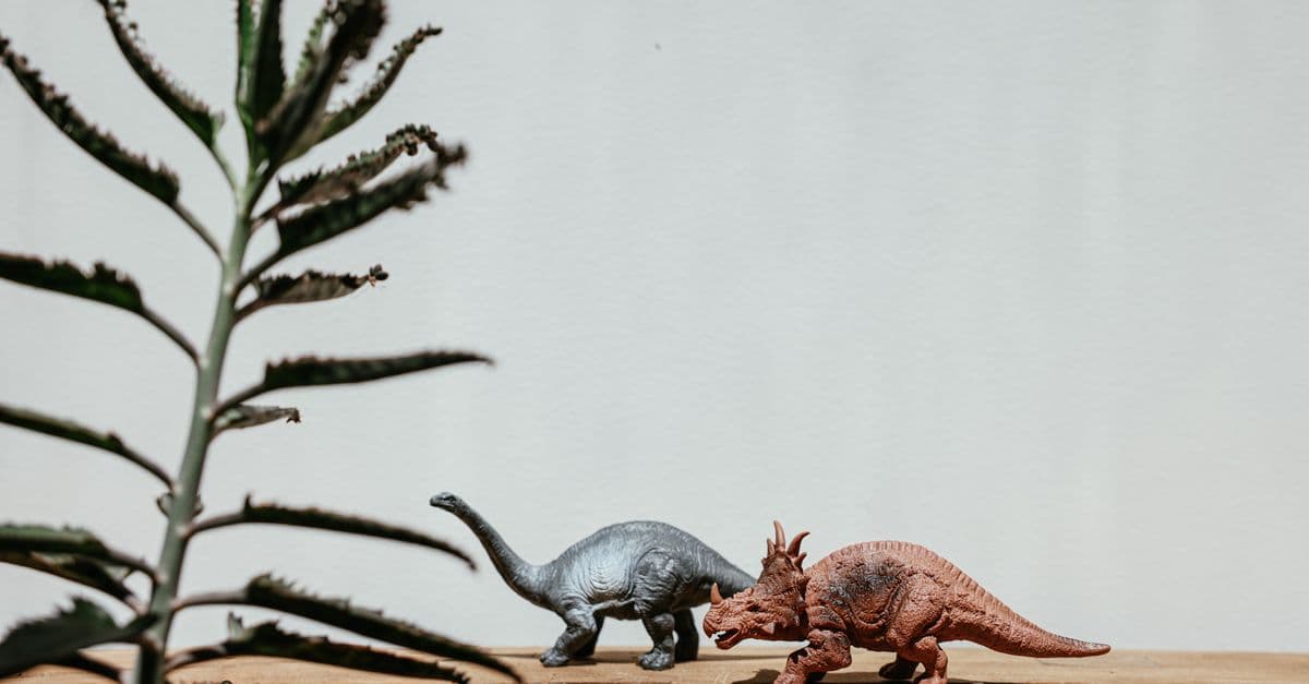 Colorful dinosaur toys with a plant on a wooden table, offering a playful prehistoric theme.