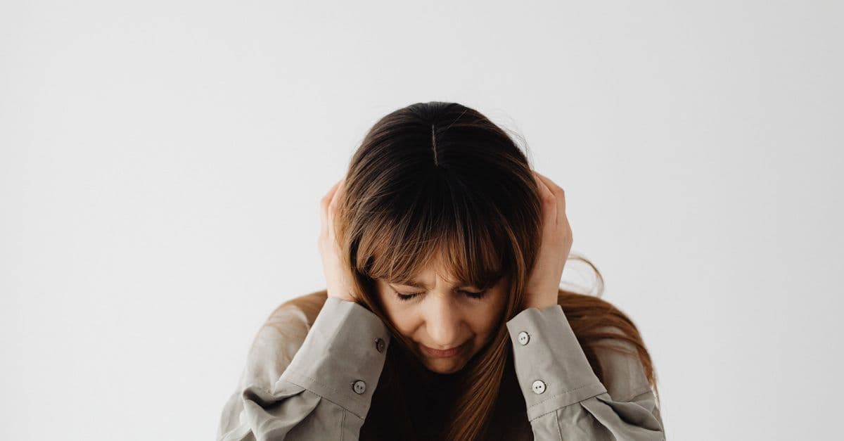 Woman with closed eyes holding head, conveying stress and emotions against a plain white background.