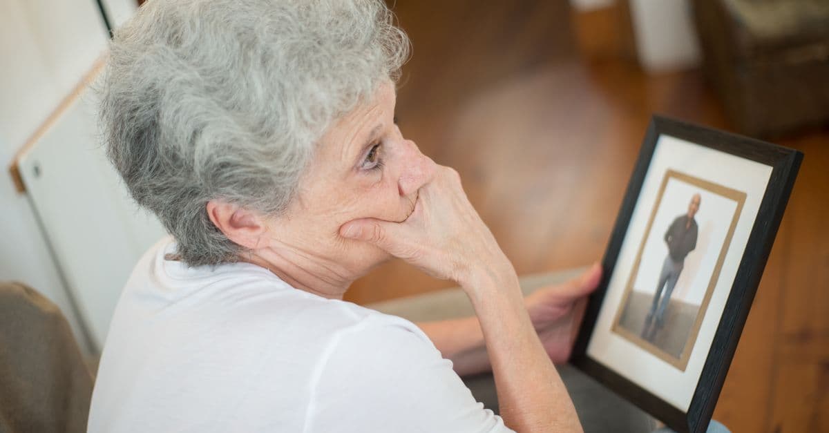 Thoughtful elderly woman with a framed photo, reflecting on memories.