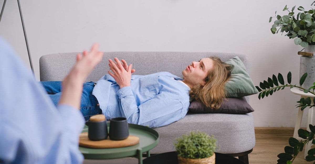 Man participating in therapy session while lying on a comfortable gray couch indoors.