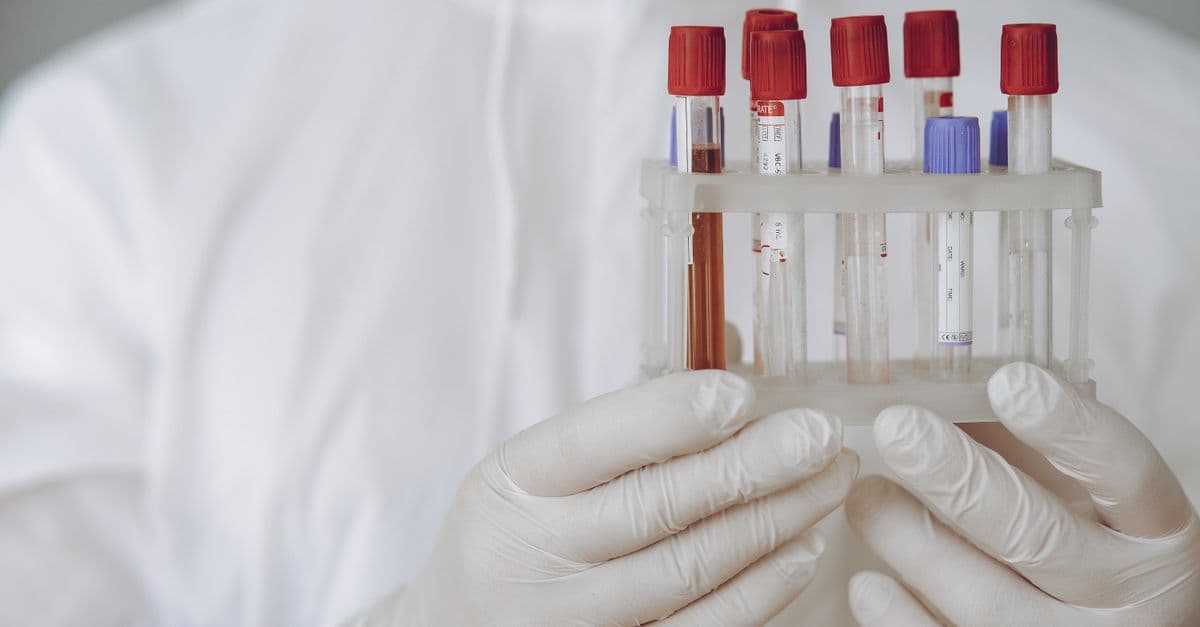 Scientist in protective gear holding test tubes in a lab setting.