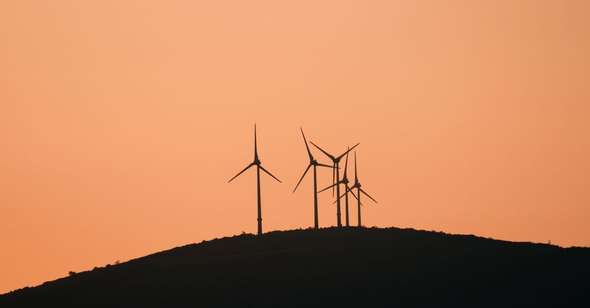 Wind turbines silhouetted against a vibrant yellow sunset sky on a rural hilltop.