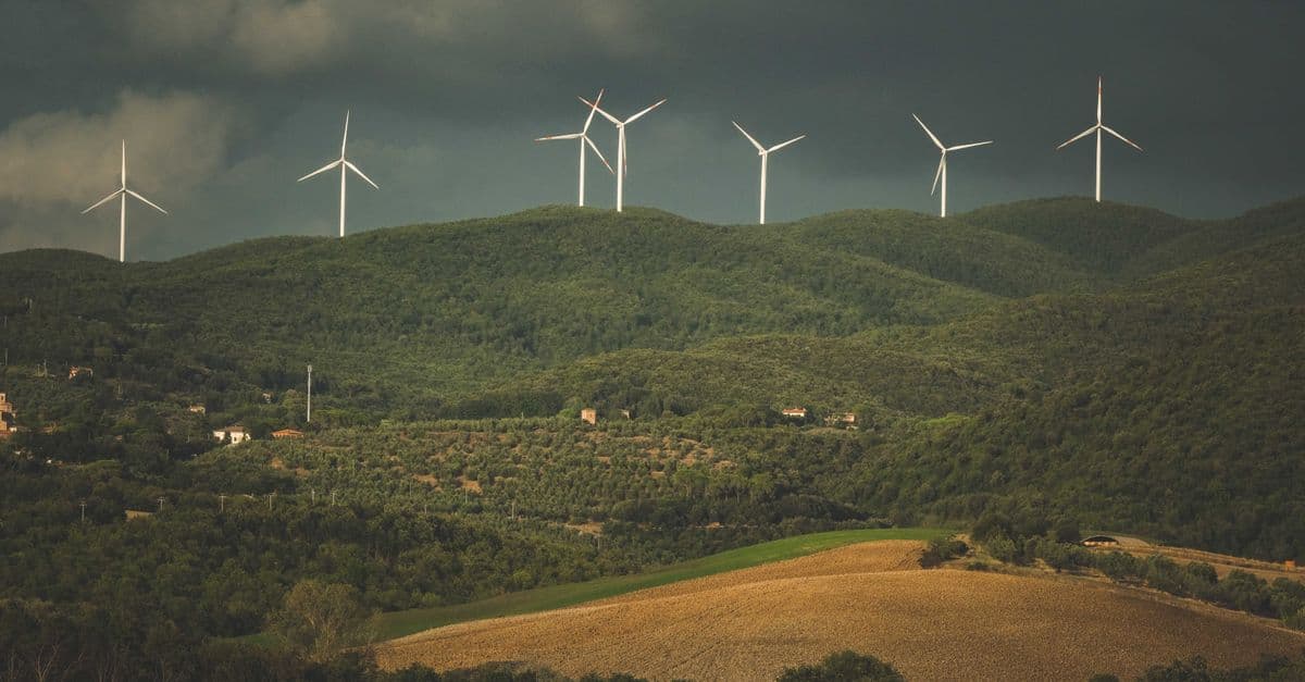 A picturesque view of wind turbines on green hills under dramatic clouds, showcasing sustainable energy.