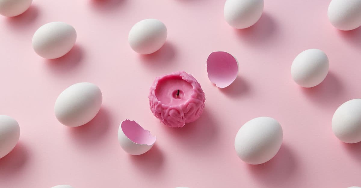 A unique pink brain-shaped candle surrounded by white eggs on a light pink backdrop, depicting creativity and contrast.