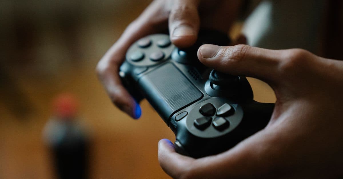 Crop anonymous male pressing buttons on console controller while playing video game in house on blurred background