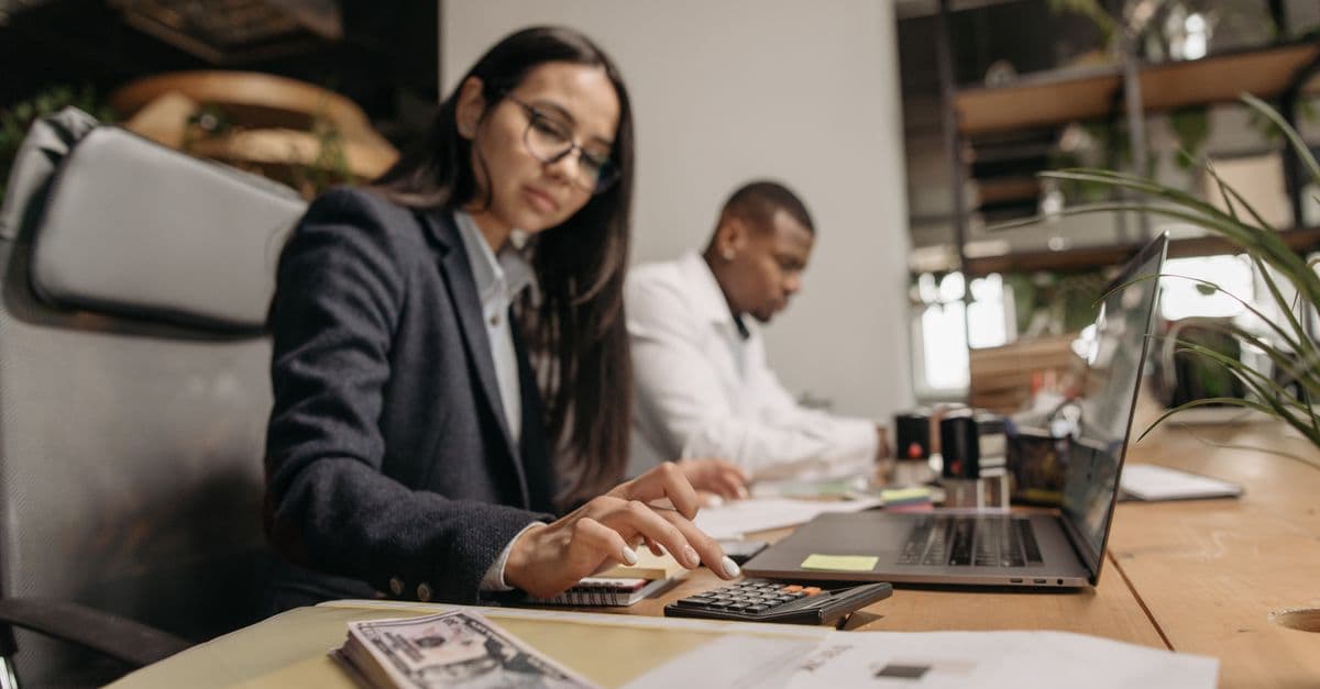 Two business professionals collaborating with a laptop and calculator in a modern office.