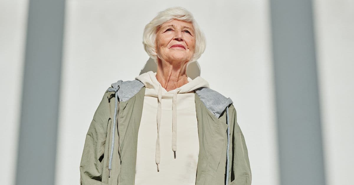 Portrait of a stylish senior woman in a coat and hoodie, embracing modern fashion outdoors.