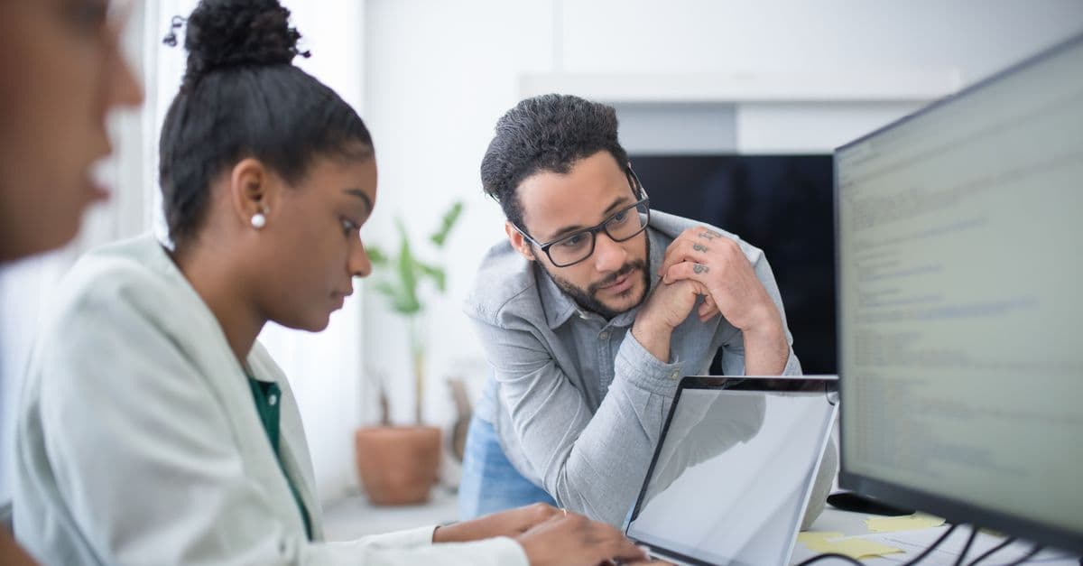 Two people collaborate in a modern office setting, focused on computer work