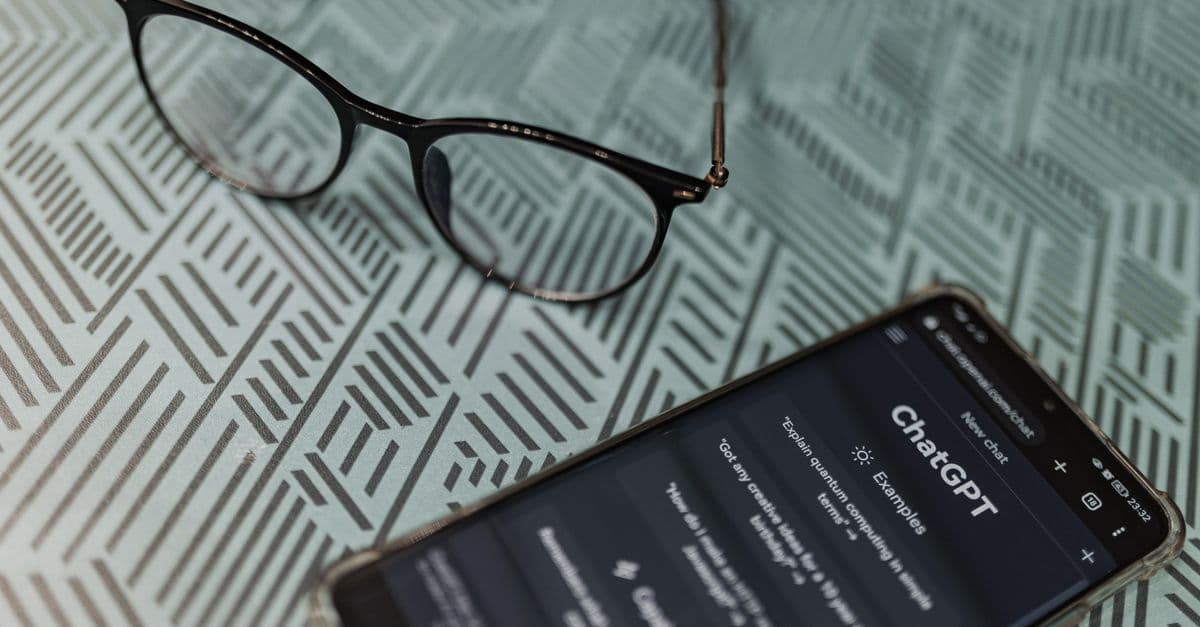 Eyeglasses next to a smartphone displaying the ChatGPT AI app on a patterned surface.