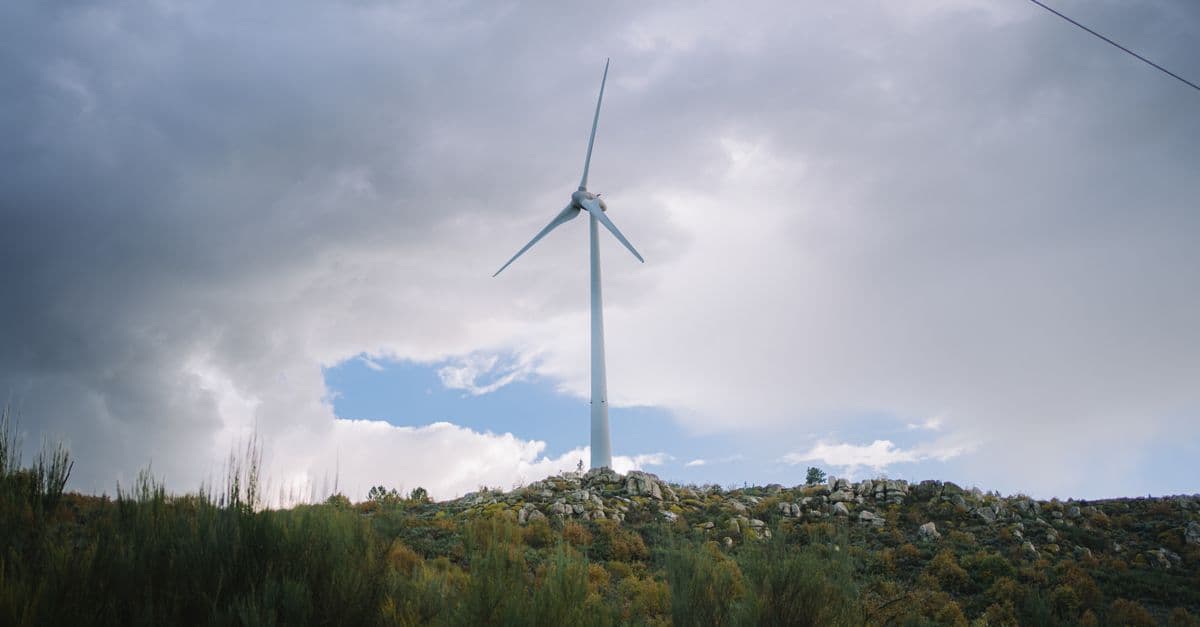 A wind turbine stands on a hill against a dramatic cloudy sky, symbolizing renewable energy.