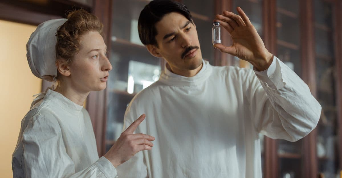 Researchers in a vintage laboratory examining a glass vial, showcasing historical scientific research.
